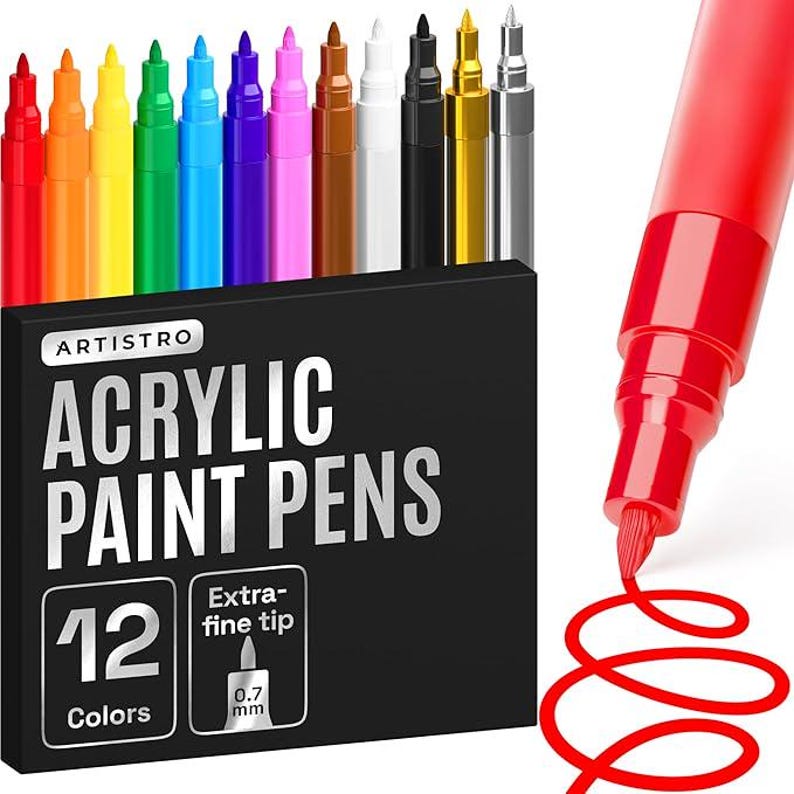 May include: A set of 12 acrylic paint pens in a black box. The pens are in various colors, including red, orange, yellow, green, blue, purple, brown, white, black, gold, and silver. The box has the text "ARTISTRO ACRYLIC PAINT PENS" and "12 Colors". The pens have an extra-fine 0.7 mm tip.