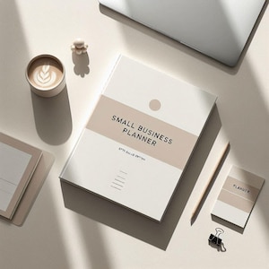 Op de afbeelding: Een crèmekleurig "Small Business Planner" boek met een lichtbruine band en tekst. Een bijpassend notitieblok, potlood, koffiekopje en paperclip liggen ook op het oppervlak. De planner heeft een minimalistisch ontwerp.