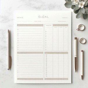 May include: A cream-colored notepad with the word "GOAL" at the top. The notepad has sections for daily tasks, priorities, and notes. Two pens and two rings are also visible.