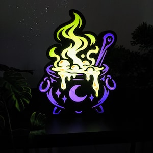 Peut inclure: Une enseigne LED lumineuse en forme de chaudron avec une base violette, un symbole de croissant de lune et des flammes jaune-vert vives s'élevant du sommet. Le design présente une cuillère et un liquide bouillonnant débordant du bord.