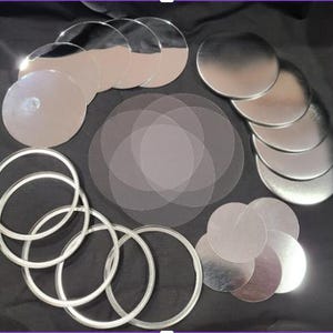May include: An assortment of silver-colored, circular metal discs and clear, circular plastic sheets. Also included are several silver-colored, circular rings. The items are arranged on a dark surface.