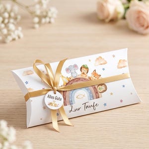 May include: White pillow box with a gold ribbon and a round tag that says "Alles Gute". The box features a rainbow, animals, clouds, and stars. The text "Zur Taufe" is printed on the box.