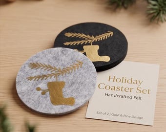 May include: A set of two round felt coasters, one light gray and one black, each featuring a gold foil print of a pine branch and a stocking. A rectangular card accompanies the coasters with the text Holiday Coaster Set Handcrafted Felt.