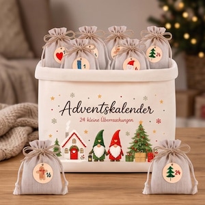 May include: A white fabric storage bin featuring the text Adventskalender 24 kleine Überraschungen, decorated with illustrations of a house, two gnomes, and a Christmas tree. It contains several small beige drawstring bags with wooden tags.