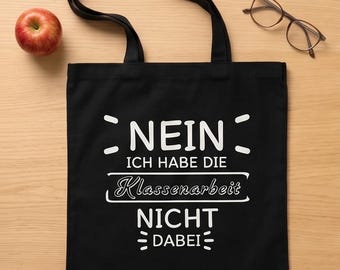 May include: Black tote bag with white text that reads "NEIN, ICH HABE DIE Klassenarbeit NICHT DABEI". A red apple and eyeglasses are next to the bag on a wooden surface. The bag has two black handles.