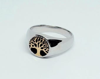 May include: A silver-colored ring with a gold-colored tree design on a round face. The ring has a smooth, polished finish and a classic signet style. The tree design is detailed and intricate.