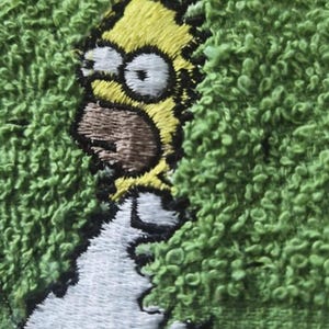 Puede incluir: Parche bordado con Homer Simpson de Los Simpson. El parche muestra la cabeza amarilla de Homer, la boca marrón y los ojos blancos, sobre un fondo verde texturizado. El diseño es detallado y colorido, adecuado para aplicar en ropa o accesorios.