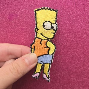 May include: Embroidered patch of Bart Simpson from The Simpsons. The patch shows Bart in his iconic orange shirt, blue shorts, and pink shoes. The patch has a yellow background with black outlines.