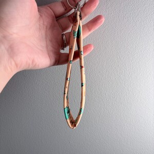 May include: A peach-colored wristlet keychain with a repeating pattern of cartoon animals in teal, blue, and red. The keychain has a silver metal clasp and a split ring for attaching keys. The wristlet is held in a hand.