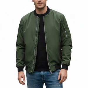 Könnte beinhalten: Olivgrüne Bomberjacke mit schwarzem Kragen, Bündchen und Saum. Die Jacke hat einen silbernen Reißverschluss und eine Reißverschlusstasche am linken Ärmel. Hergestellt aus einem glatten, leichten Material.