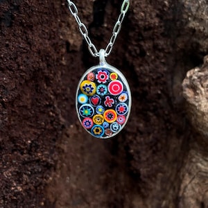 Puede incluir: Collar con colgante ovalado y cadena plateada. El colgante presenta un diseño de mosaico colorido con patrones florales y geométricos en rojo, amarillo, azul y negro. El colgante mide aproximadamente 3,8 cm de largo.