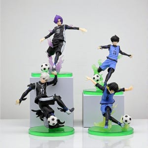 May include: Four soccer player figurines in dynamic poses, each with a soccer ball. The figures wear black and blue uniforms with numbers. They stand on green bases with translucent flame-like accents.