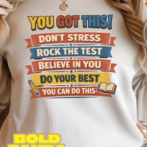 May include: Cream-colored sweatshirt with the text "YOU GOT THIS!" in yellow and red. Below, the shirt features the phrases "DON'T STRESS", "ROCK THE TEST", "BELIEVE IN YOU", "DO YOUR BEST", and "YOU CAN DO THIS". A pencil and book graphic are also included.