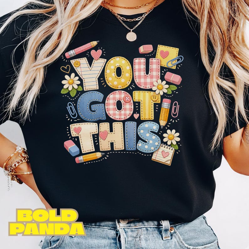 May include: Black t-shirt with the phrase "YOU GOT THIS" in colorful, patterned letters. The design includes pencils, erasers, hearts, and flowers, creating a cheerful, school-themed graphic.