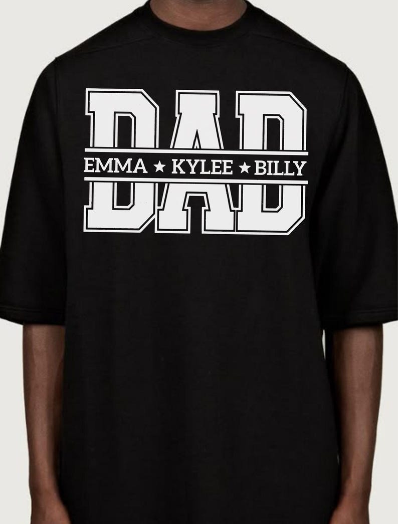 May include: Black t-shirt featuring the word "DAD" in large white block letters. Underneath, the names "EMMA", "KYLEE", and "BILLY" are displayed in white. The shirt has short sleeves.