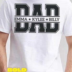 May include: White t-shirt featuring the word "DAD" in large, black, block letters. Underneath, the names "EMMA", "KYLEE", and "BILLY" are displayed with star separators. The shirt has short sleeves.