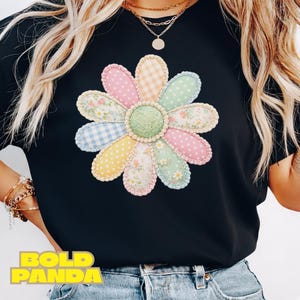 May include: Black t-shirt featuring a large, colorful flower design. The flower has pastel petals with various patterns, including polka dots, gingham, and floral prints. The text "BOLD PANDA" is printed in yellow at the bottom.