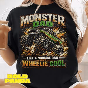 Puede incluir: Sudadera negra con un gráfico de un camión monstruo verde con el texto "MONSTER DAD" y "WHEELIE COOL". El diseño presenta acentos naranjas y amarillos, y también se incluye el texto "LIKE A NORMAL DAD BUT".