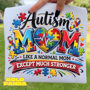 May include: White t-shirt with the words "Autism Mom" in colorful puzzle piece letters and a heart-shaped puzzle design. The shirt also has the text "Like a normal mom except much stronger" in a banner.