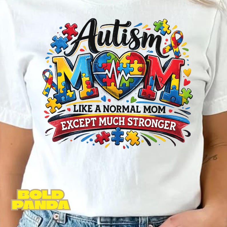 May include: White t-shirt with a colorful graphic design. The design features the words "Autism Mom" in a stylized font, with puzzle pieces and a heart-shaped element. The text "Like a normal mom except much stronger" is also included.