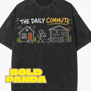 May include: Dark gray t-shirt with a graphic that reads "THE DAILY COMMUTE." The design features a house, a person with a coffee cup, and a garage with tools. The text "BOLD PANDA" is at the bottom.