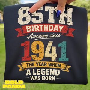 Puede incluir: Camiseta azul marino con el texto "85 cumpleaños Awesome since 1941". La camiseta también dice "The year when a legend was born" en un estilo vintage.