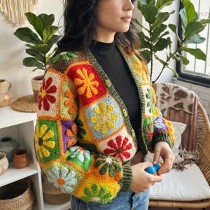 May include: A vibrant crochet cardigan with a patchwork design. It features flower motifs in various colours, a green trim, and button closure. The sleeves are long, and the style is bohemian. The cardigan is a unique, handmade garment.