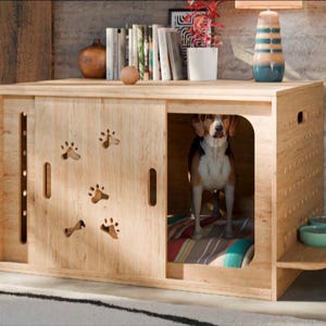 Può includere: Una cuccia per cani in legno chiaro dotata di porta scorrevole con impronte di zampe ritagliate, un ripiano laterale con due piccole ciotole e uno spazio interno con un cuscino a righe dove si trova un beagle.