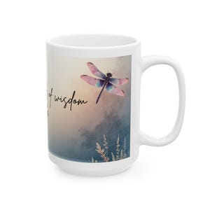 May include: White ceramic mug with a dragonfly design. The dragonfly has pink and blue wings, and the mug has the words "a cup of wisdom" written on it. The background is a soft blend of colors.