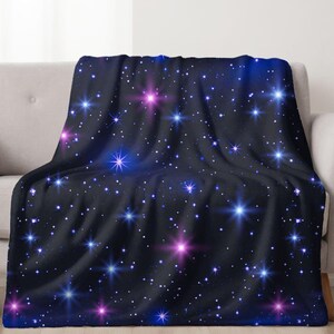 May include: A soft, plush throw blanket with a dark blue background and a scattered pattern of white, pink, and blue stars. The stars are of varying sizes and have a glowing effect.
