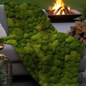 May include: A green moss throw blanket with a textured surface. The blanket is draped over a gray couch with a pillow and a side table with a candle.