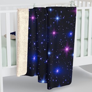 Puede incluir: Una manta suave y mullida con un fondo azul oscuro y un patr&oacute;n repetitivo de estrellas blancas y azules. Las estrellas tienen un efecto brillante, algunas estrellas son rosadas y otras azules.