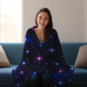 Puede incluir: Una persona est&aacute; sentada en un sof&aacute; envuelta en una suave manta de franela azul con un estampado de galaxia con estrellas blancas, azules y rosas.