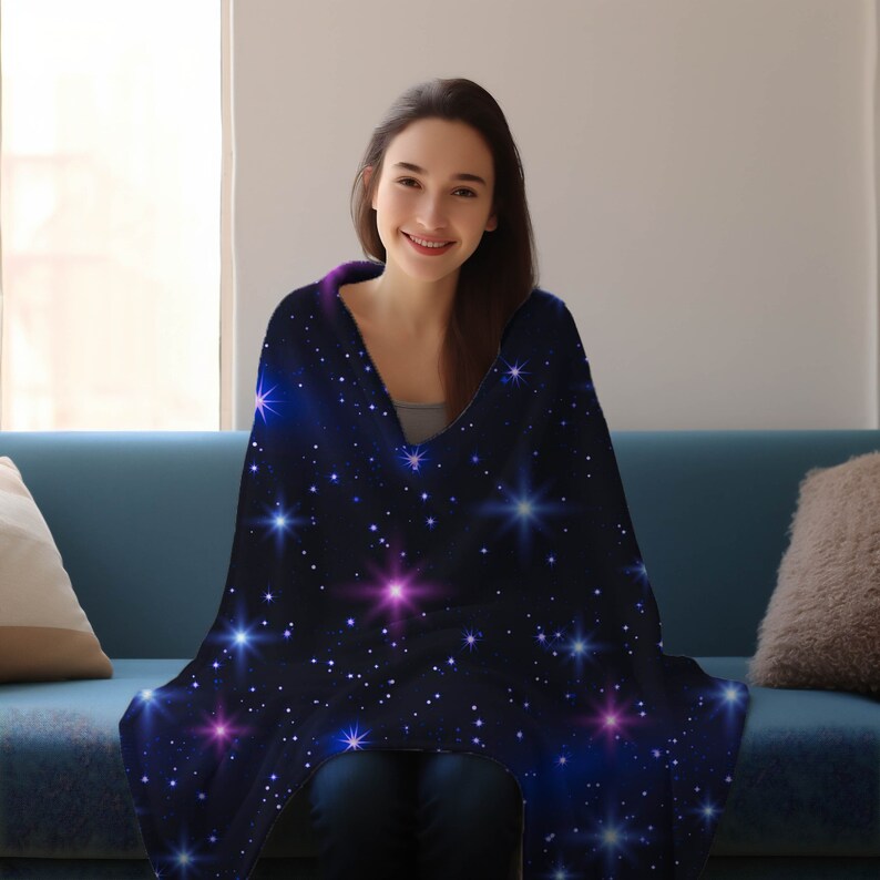 Puede incluir: Una persona est&aacute; sentada en un sof&aacute; envuelta en una suave manta de franela azul con un estampado de galaxia con estrellas blancas, azules y rosas.