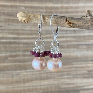 Puede incluir: Un par de pendientes de plata con una perla rosa y un racimo de pequeñas piedras preciosas rosas.