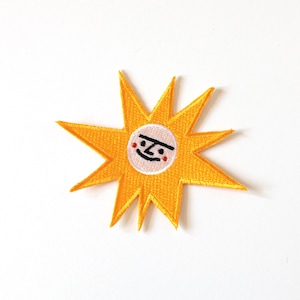 May include: Embroidered yellow sun patch with a smiling face. The sun has eight pointed rays and a white circle in the center with a simple face design. This patch is perfect for adding to clothing or accessories.