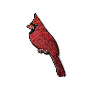 May include: Embroidered patch featuring a vibrant red cardinal bird. The patch has a detailed design with a black outline, showcasing the bird's features. The cardinal is perched, with its crest and beak clearly visible, perfect for adding to clothing or accessories.