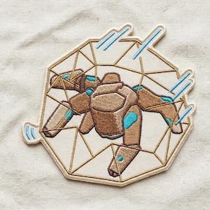May include: Embroidered patch featuring a geometric design with a brown robotic insect inside a white and gold geometric shape. The insect has blue accents, and the patch is on a cream-colored fabric.