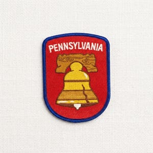 May include: A Pennsylvania patch featuring a red background with a blue border. The patch displays a gold Liberty Bell and a wooden beam, with the word "PENNSYLVANIA" in white lettering.