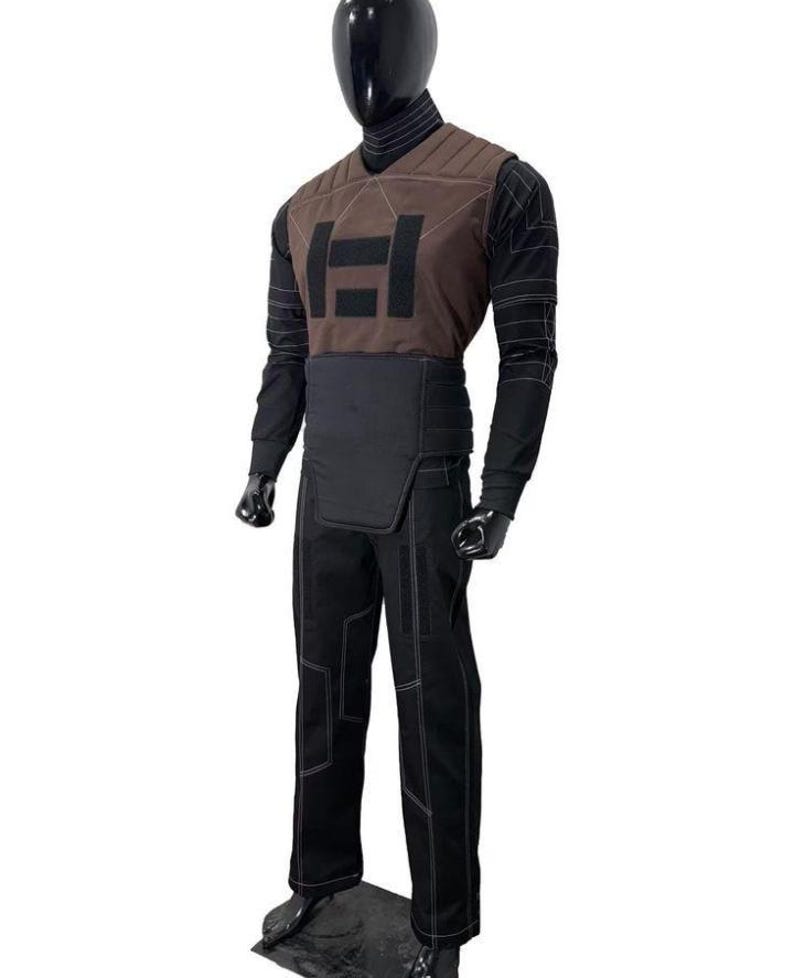 May include: A costume set featuring a brown V-neck vest with a black rectangular emblem, worn over a black long-sleeve shirt with white geometric stitching. The outfit includes a black waist belt and matching black trousers with white line details.