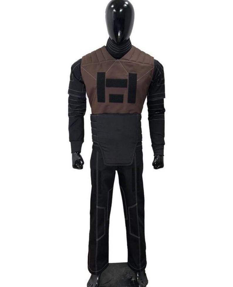 May include: A full-body costume displayed on a mannequin, featuring a brown chest piece with black rectangular patches, a black long-sleeved shirt with ribbed detailing, a black waist guard, and black trousers with visible white stitching throughout.