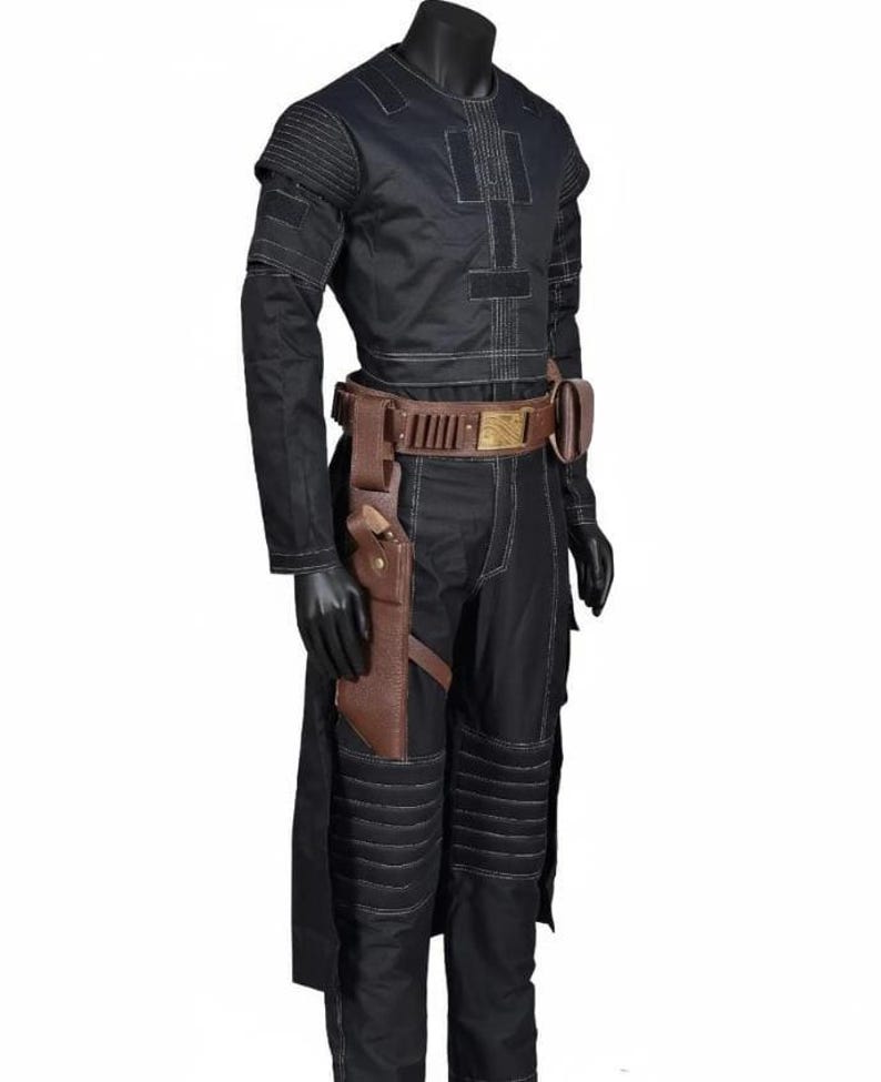 May include: Black costume with white stitching, featuring a long-sleeved top, pants, and a brown belt with a holster. The costume has a military-inspired design with padded details on the shoulders and knees. The belt has a gold-colored buckle.