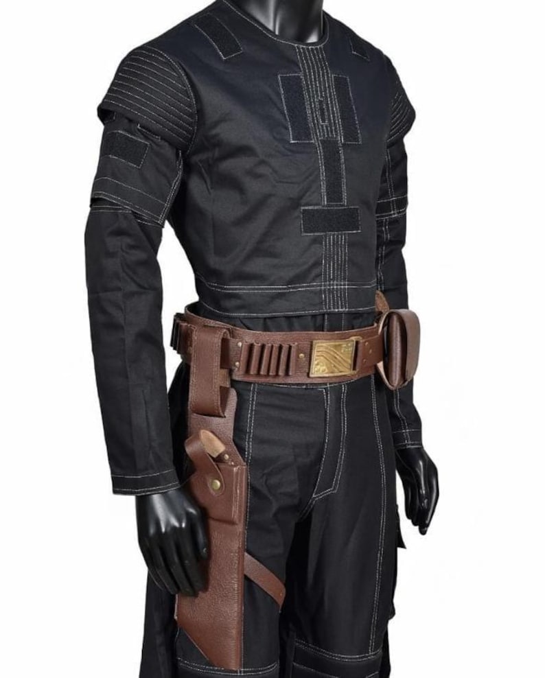 May include: Black costume with white stitching, featuring a utility belt with pouches and a holster. The outfit includes a long-sleeved top and pants. The belt has a gold-colored buckle.