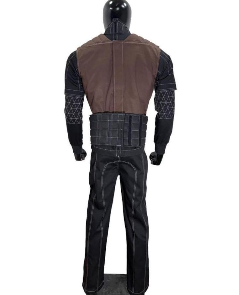 May include: A full-body costume set featuring a black long-sleeved shirt with white geometric grid patterns on the sleeves, a brown vest with quilted shoulder detailing, a black tactical-style waist belt, and matching black trousers with white stitching.