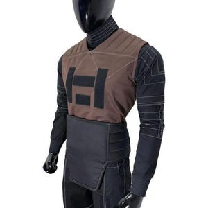 May include: A black long-sleeved shirt with white pinstripes worn under a brown quilted vest featuring a black rectangular patch design. A black padded waist belt is worn over black trousers with white stitching details on a mannequin.