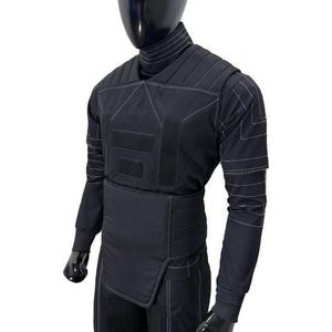 May include: Black protective suit with white stitching details, displayed on a mannequin. The suit features a high collar, quilted panels, and multiple Velcro closures. The long-sleeved top and pants are designed for full body coverage.