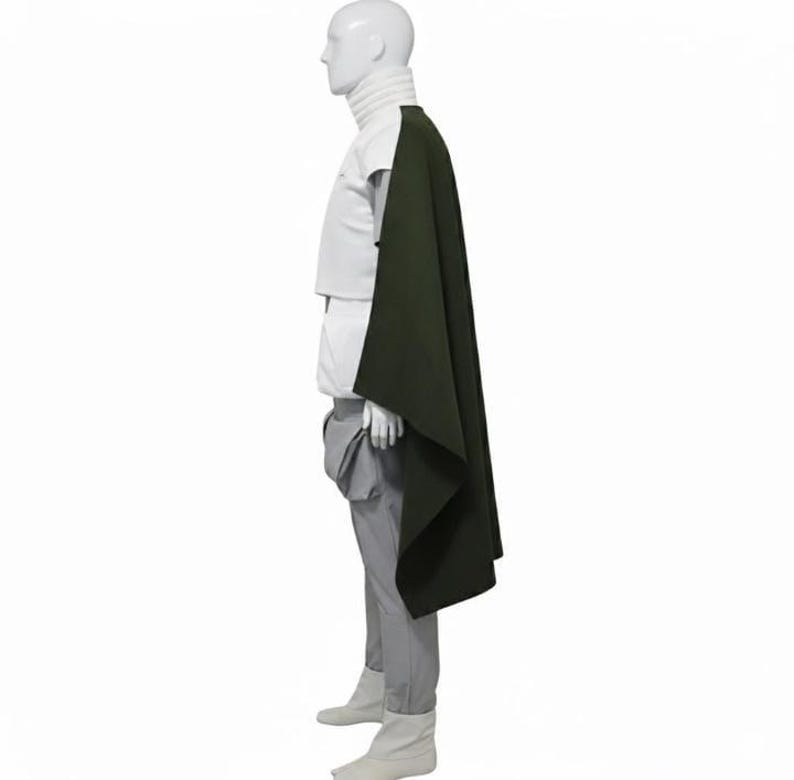May include: A mannequin wearing a white turtleneck, white short-sleeved shirt, gray pants, and white boots. A dark green cape is draped over the mannequin's shoulder. The outfit is displayed against a white background.