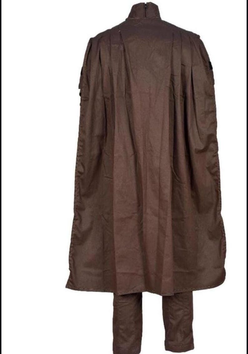 May include: A brown outfit consisting of a long cape and matching pants. The cape has a high collar and extends to the knees. The pants are straight-legged. The outfit is made of a solid, matte fabric.