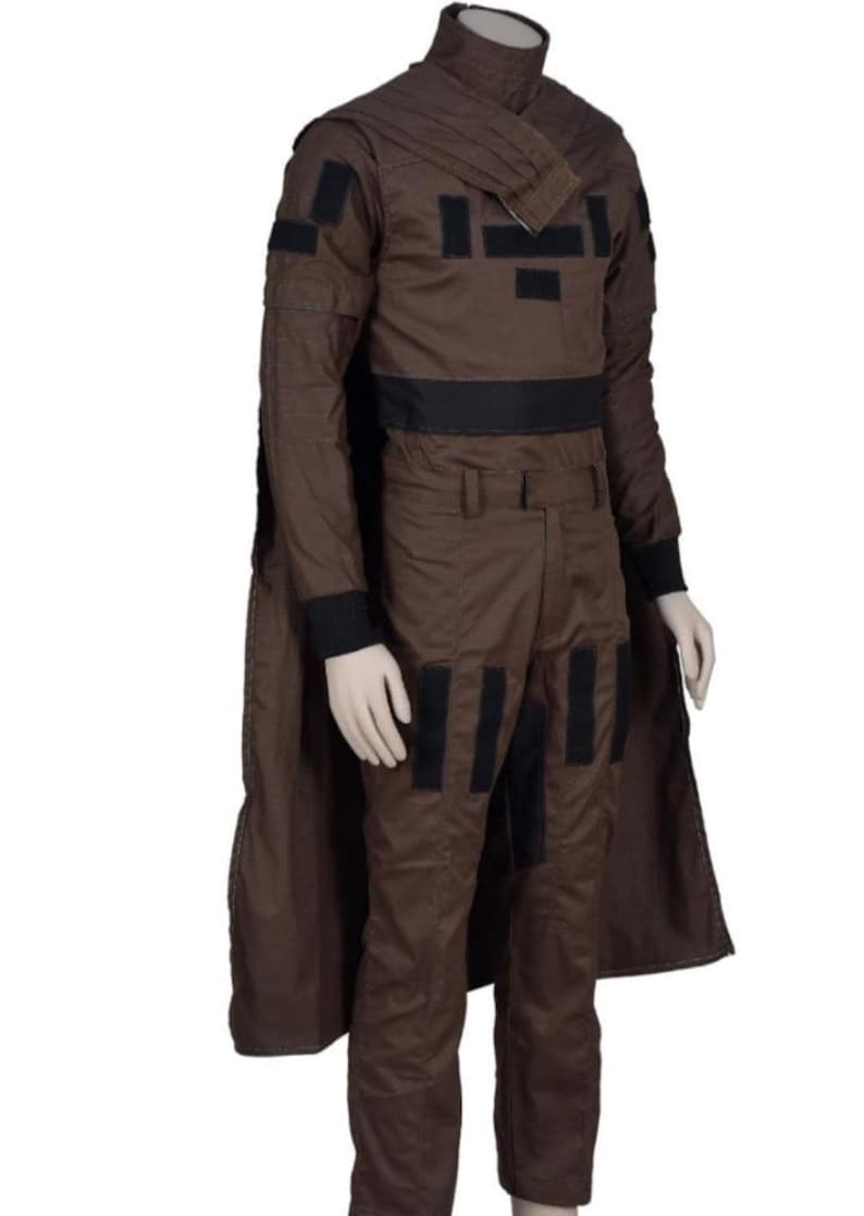 May include: Brown costume with black accents, featuring a high collar and a cape. The outfit includes a long-sleeved top with black patches and a black belt, along with matching pants. The costume is designed with a military or sci-fi aesthetic.