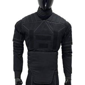May include: Black tactical vest with white stitching details, displayed on a mannequin. The vest features multiple panels, hook-and-loop closures, and long sleeves. The mannequin is wearing a black turtleneck and pants.